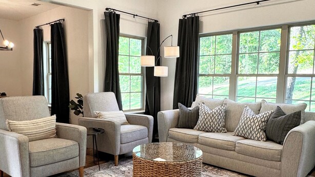 A living room with a sofa, armchairs, a coffee table, and a large window with curtains.