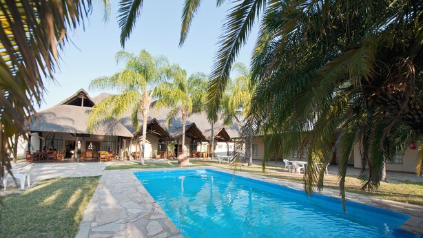 Una piscina rodeada de baldosas de piedra, palmeras y un edificio con varias habitaciones.