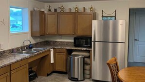 Una cocina con armarios de madera, un refrigerador de acero inoxidable, un microondas y un bote de basura.