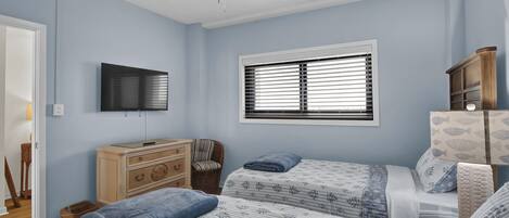 Quarto com duas camas, ventoinha no teto, televisão, janela com persianas, cómoda e uma cadeira.