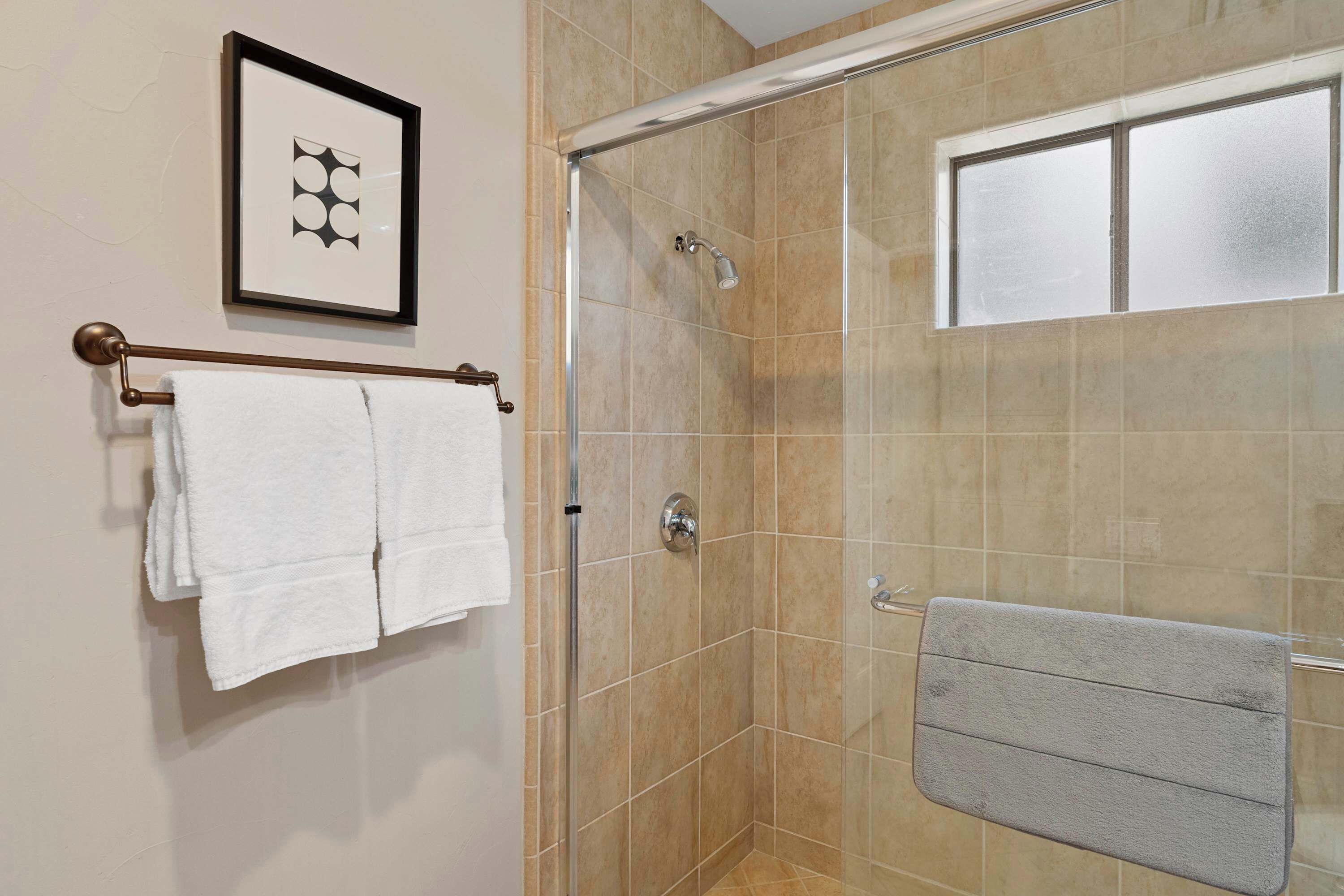 A shower area with a glass door, a towel rack with two white towels, and a framed picture on the wall.