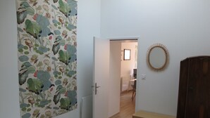 A bedroom with a bed, a wooden bench, a mirror, and a door leading to another room. - Rose Garden Bayeux (Bayeux)