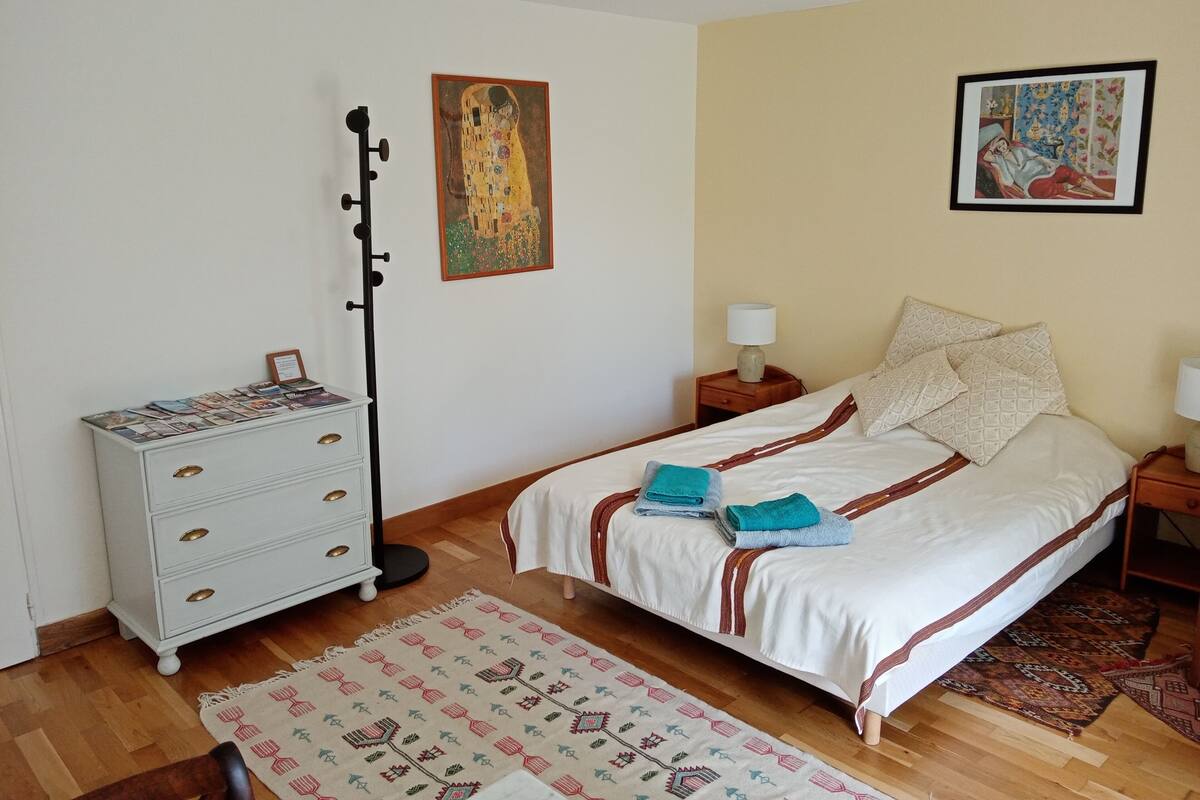 A bedroom with a bed, a dresser, a lamp, and two paintings on the wall.