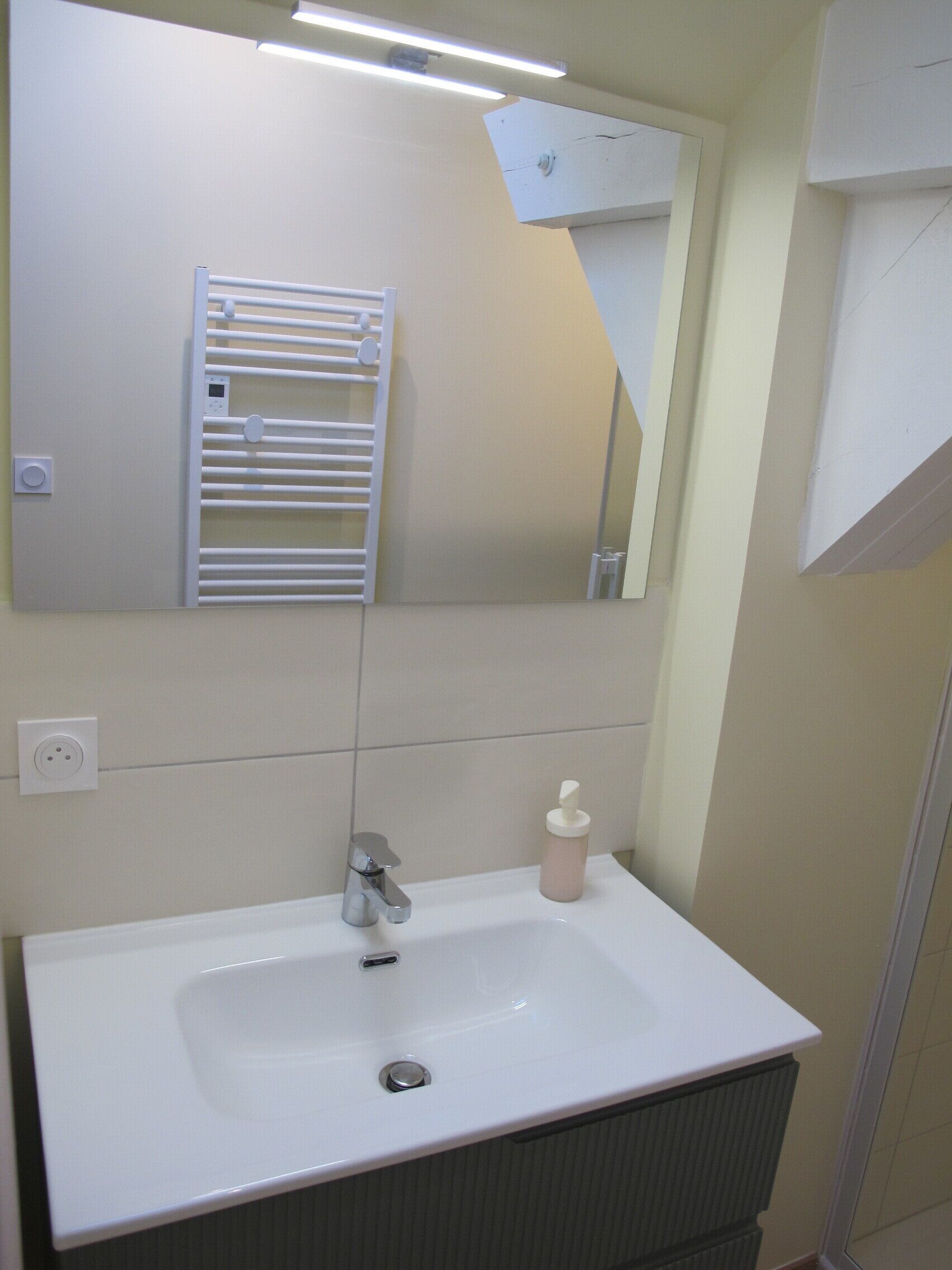 Un baño con lavamanos blanco, un espejo, toallero y dispensador de jabón.