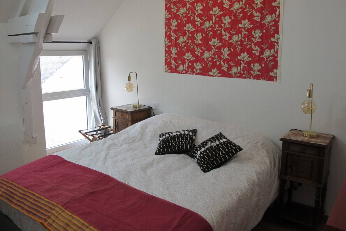 A bedroom with a bed, two bedside tables, a window, and a red floral tapestry on the wall.
