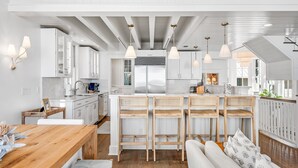 Una cocina moderna con armarios blancos, una mesa de comedor de madera y una barra con taburetes.