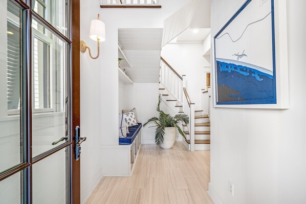 A hallway with a wooden bench, a potted plant, and a staircase with white railings.