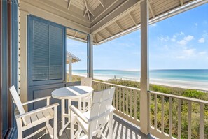 A covered balcony with a table and chairs, overlooking a beach.