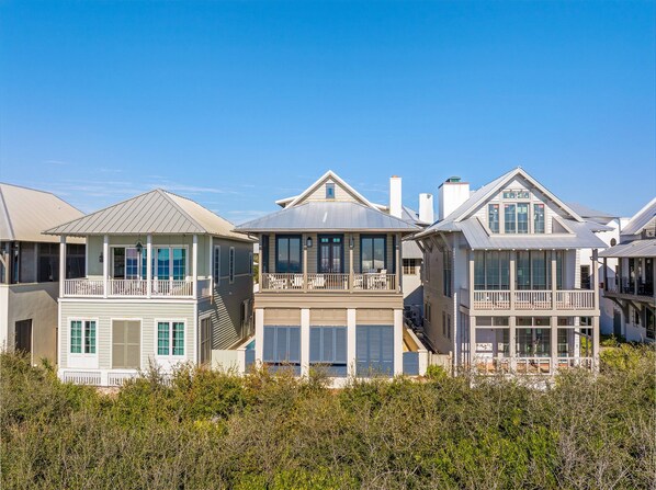 A row of coastal houses with balconies, large windows, and a clear blue sky.