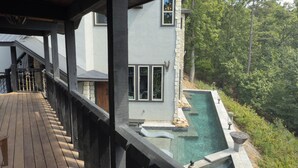 A modern house with a wooden deck, a stone wall, and a clear swimming pool.