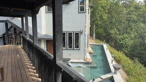 A modern house with a wooden deck, a stone wall, and a clear swimming pool.