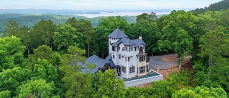 A large, multi-story house surrounded by dense forest, with a clear view of the surrounding landscape.