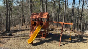 A wooden play structure with a slide in a forested area.