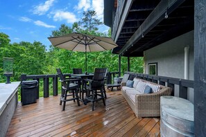Een terras buiten met een tafel, stoelen, een rieten bank en een parasol.