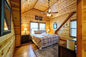 A cozy bedroom with a bed, bedside lamps, a ceiling fan, and wooden walls. - # Time Well Spent  ## Luxury Broken Bow Cabin with Hot Tub, Creek, Playground, a (Broken Bow)