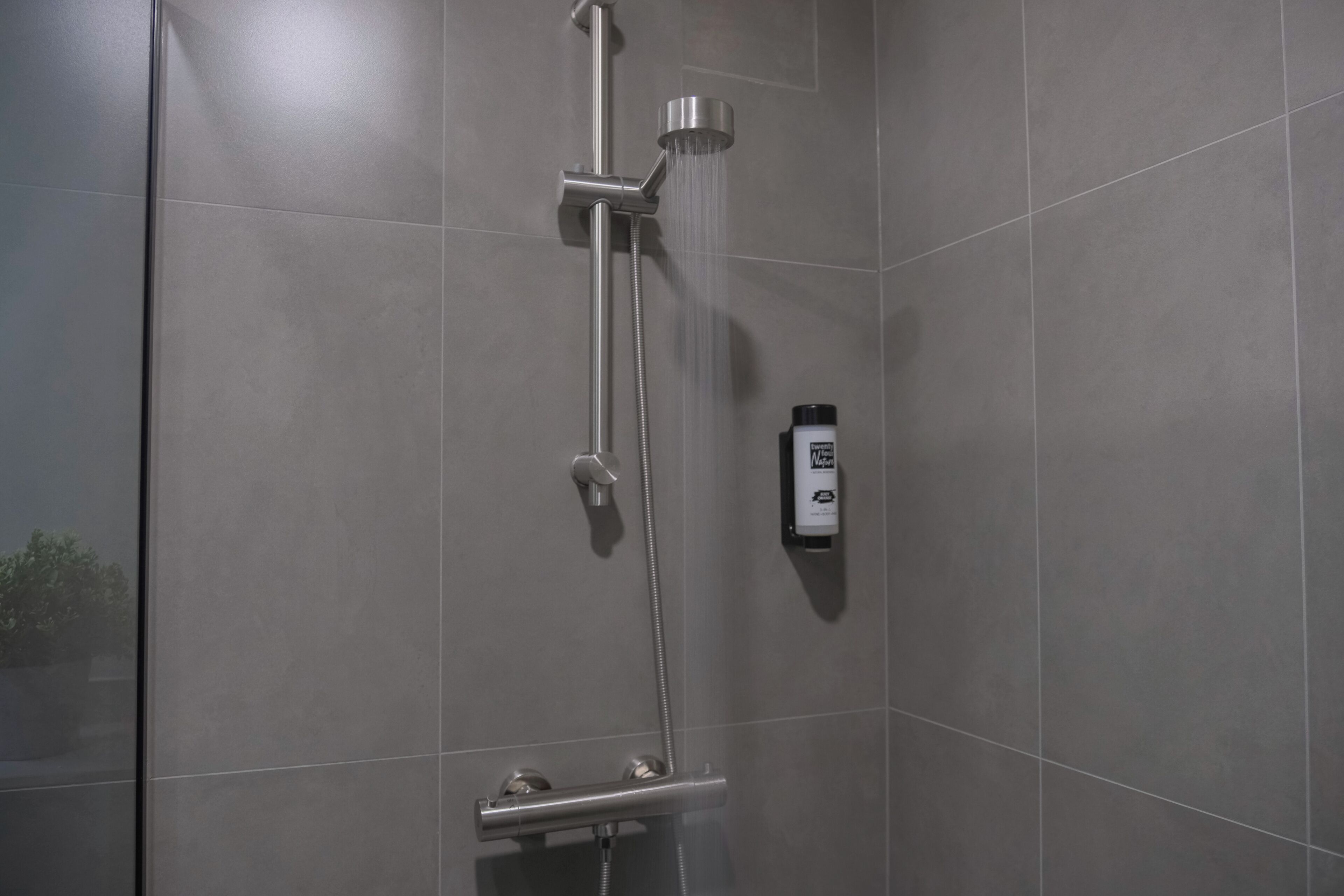 A modern shower with a handheld showerhead and a fixed showerhead, a handheld soap dispenser, and a wall-mounted soap dispenser.