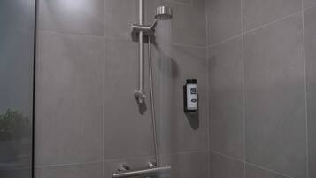 Eine moderne Dusche mit Handbrause und fest installierter Duschkopf, einer Handseifenspender sowie einem wandmontierten Seifenspender.