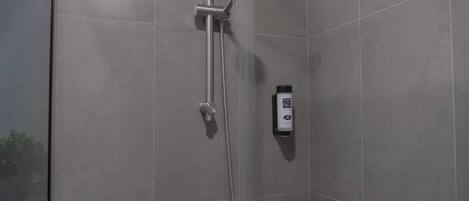 A modern shower with a handheld showerhead and a fixed showerhead, a handheld soap dispenser, and a wall-mounted soap dispenser.