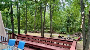 A wooden deck with glass-top tables and chairs, overlooking a forested area. - Spacious 4BR Escape in Sherwood Forest (Grayling)