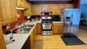A kitchen with wooden cabinets, stainless steel appliances, a sink, and a refrigerator. - Spacious 4BR Escape in Sherwood Forest (Grayling)