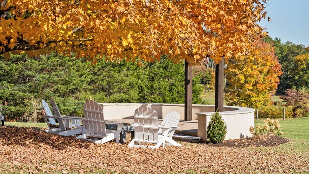 An outdoor seating area with Adirondack chairs and a table under a large tree with yellow leaves. - Afton Mountain Vineyards (Afton)