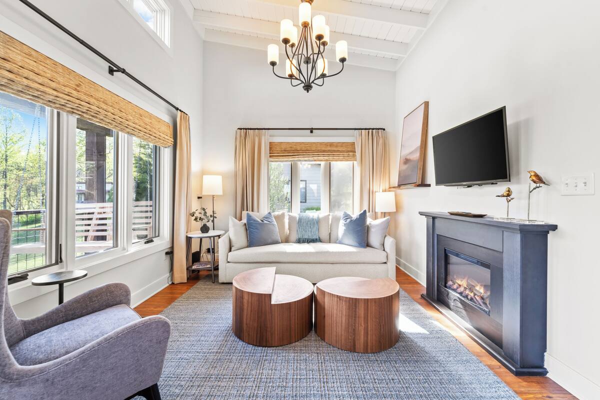 A modern bedroom with a large bed, a fireplace, a television, and a view of the outdoors.