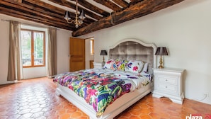 Ein Schlafzimmer mit einem großen Bett, Holzbalken, einem Fenster und einem Fliesenboden.