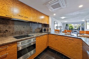 Eine moderne Küche mit Holzausbau, einem eingebauten Mikrowellenherd, Edelstahlgeräten und einer großen Kochinsel mit Spüle.
