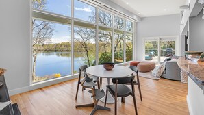 A modern kitchen with a large window overlooking a lake, a dining area with a round table, and a cozy seating area with a view of the outdoors. - Majestic lakefront 3-bedroom with pool, hot tub, water sports and birdwatching (Arlington)