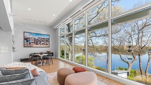 A modern living room with a large window overlooking a lake, a dining area, and a cozy seating arrangement. - Majestic lakefront 3-bedroom with pool, hot tub, water sports and birdwatching (Arlington)