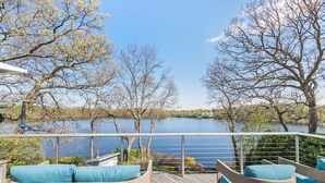 A wooden deck with outdoor seating and a view of a lake. - Majestic lakefront 3-bedroom with pool, hot tub, water sports and birdwatching (Arlington)