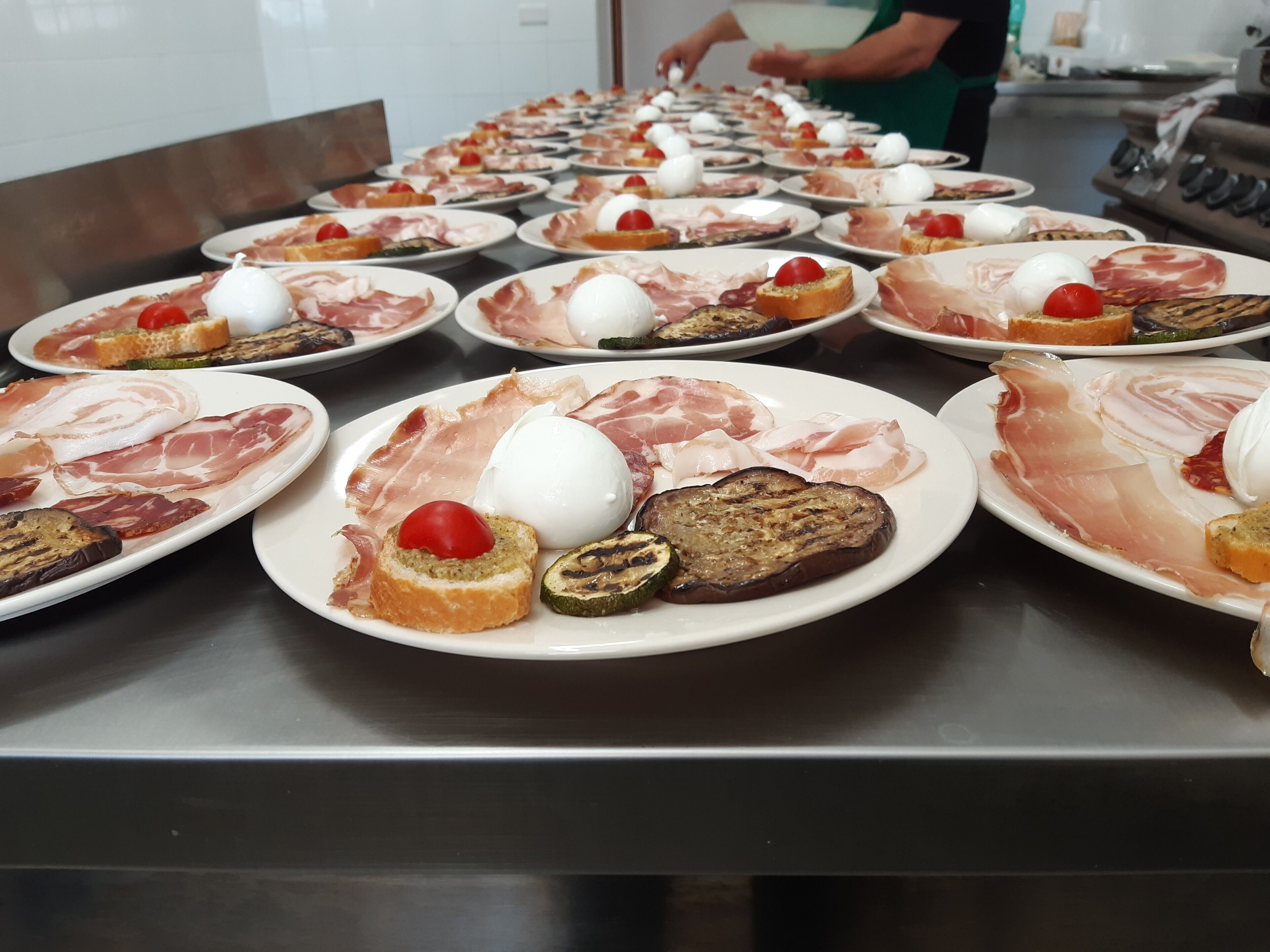 Una mesa de buffet con diferentes platos de comida, incluyendo jamón serrano, mozzarella y verduras a la parrilla.