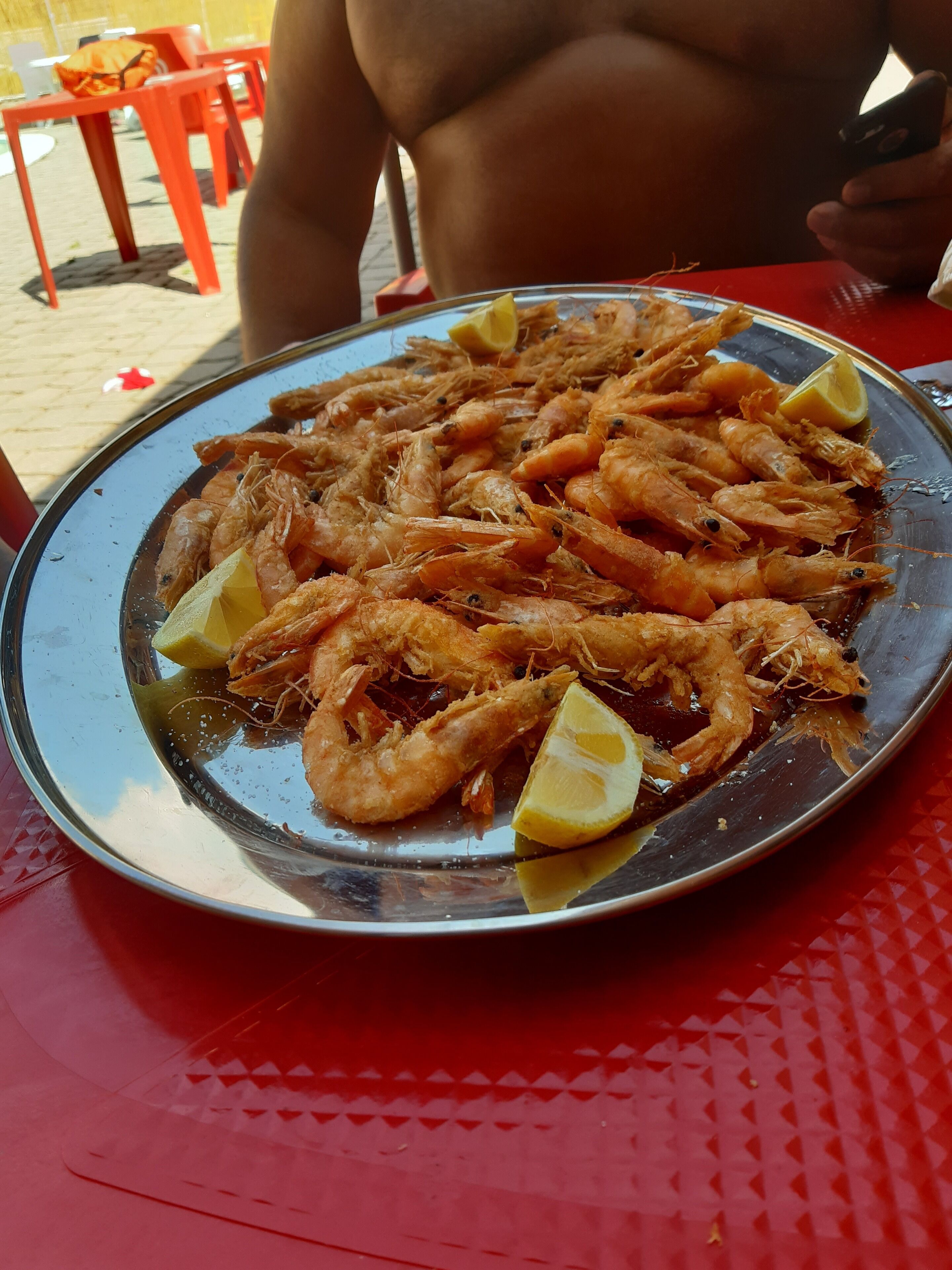 A plate of cooked shrimp with lemon wedges on a metal tray.