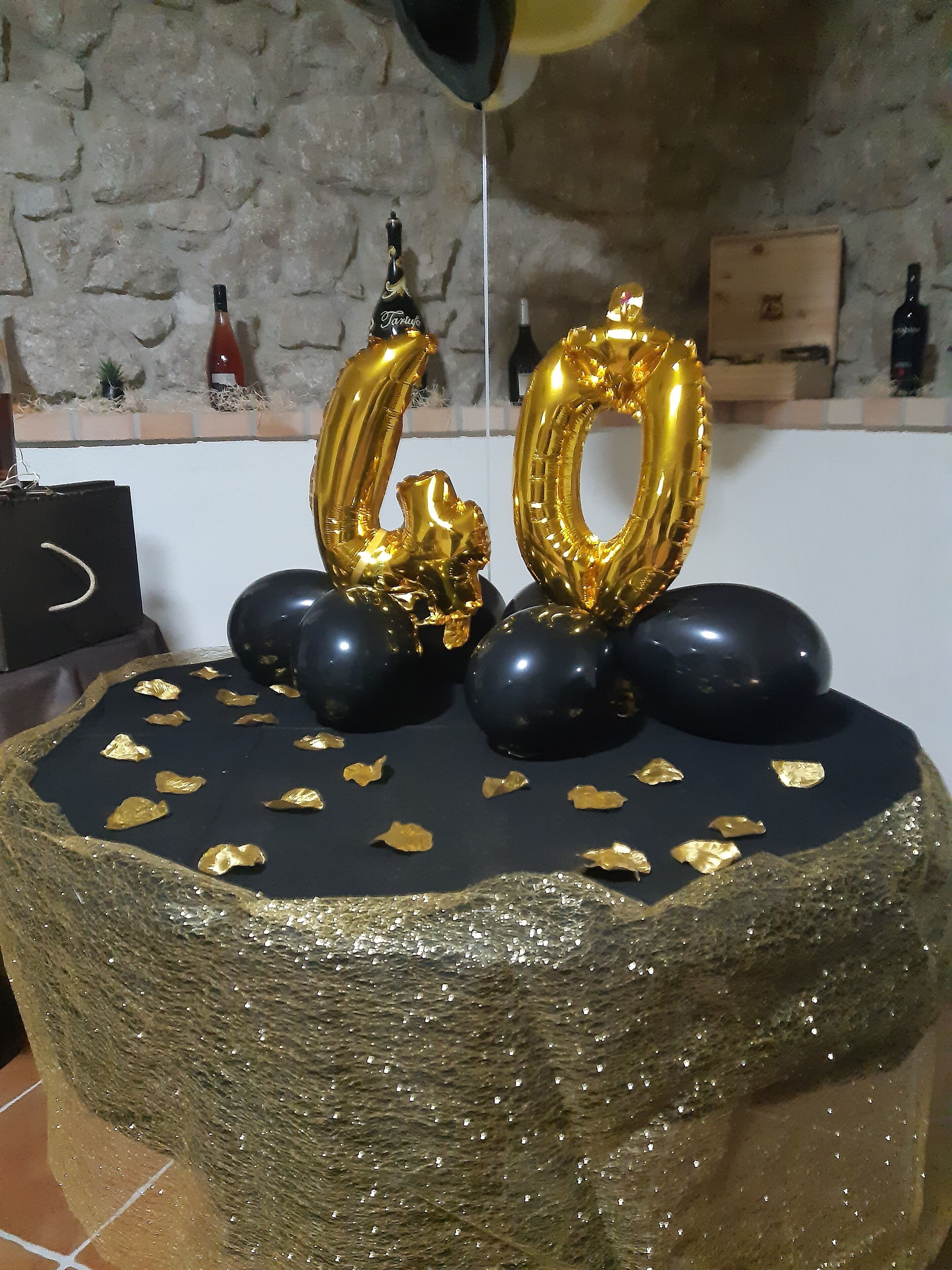 A cake with gold and black decorations, including two gold balloons shaped like numbers 60, placed on a textured surface.