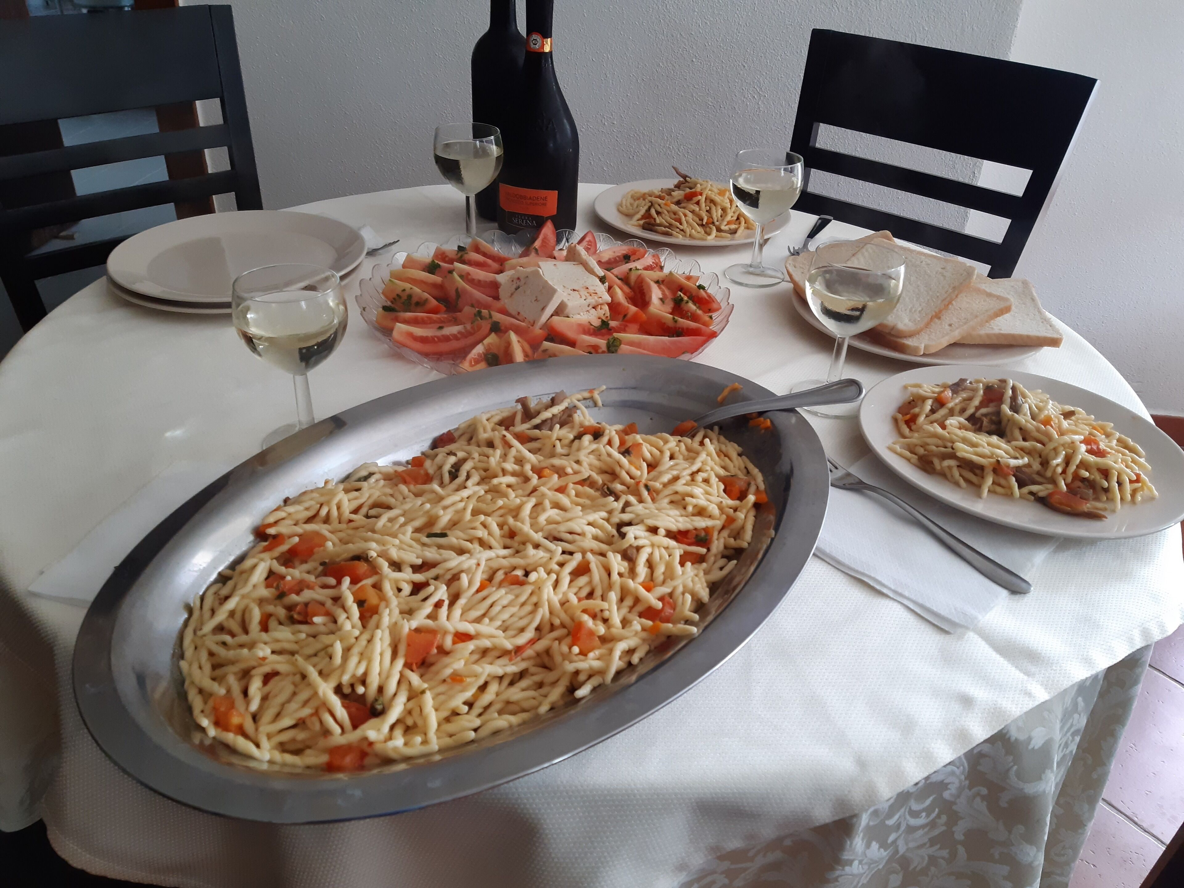 A dining table with various dishes, including pasta, bread, and a bottle of wine.