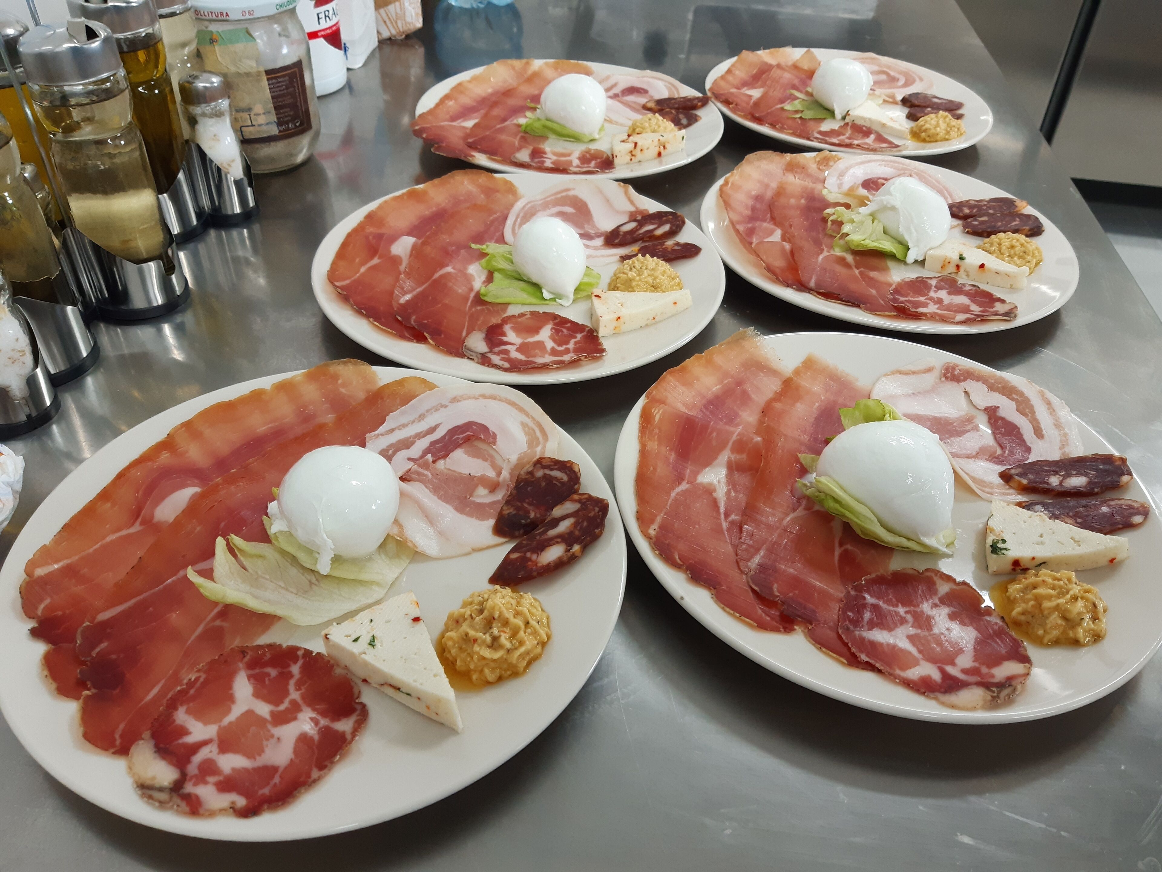 A table with plates of food, including prosciutto, cheese, and olives.