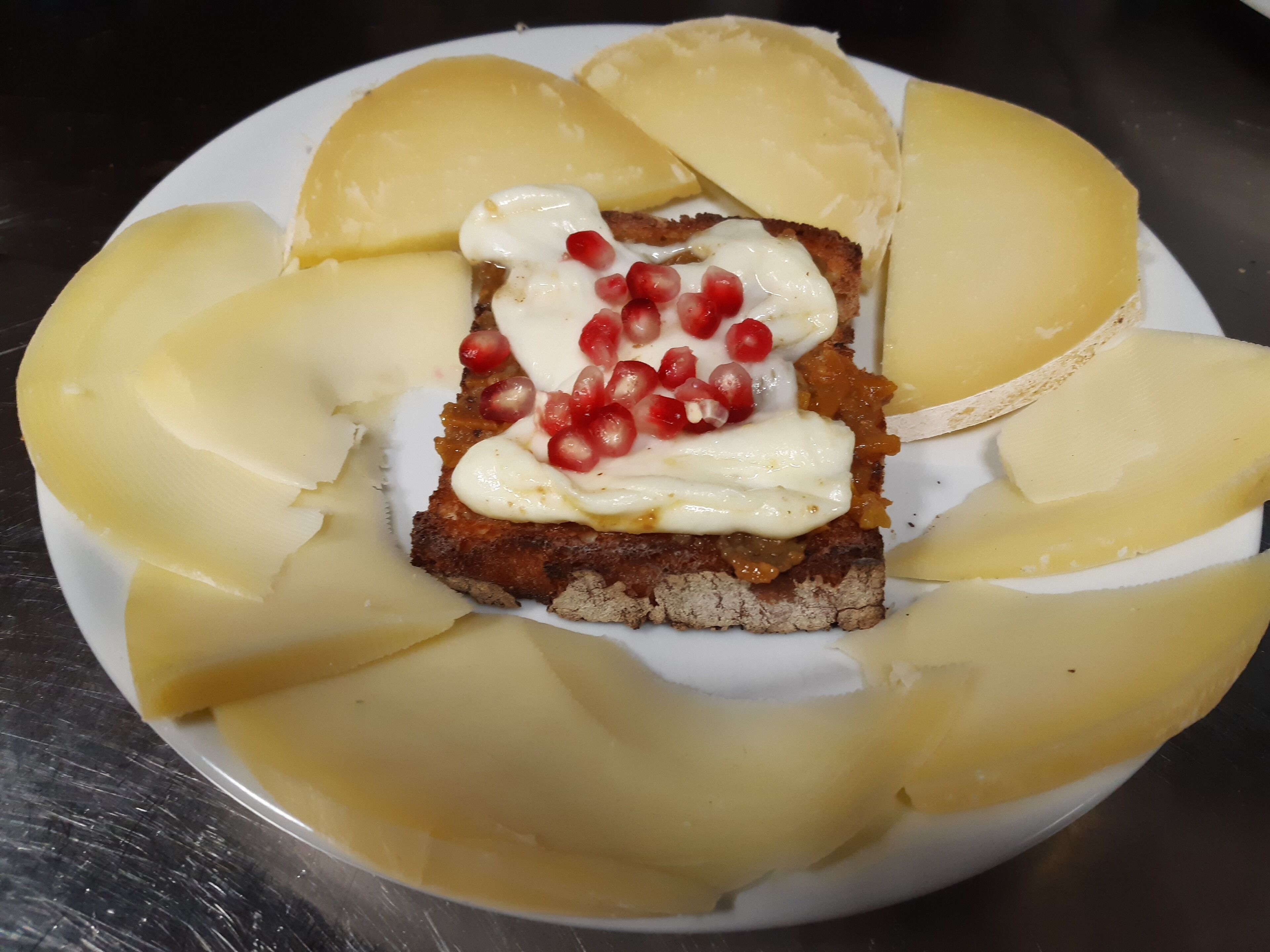 A plate with a slice of bread topped with cream and pomegranate seeds, surrounded by slices of yellow fruit.