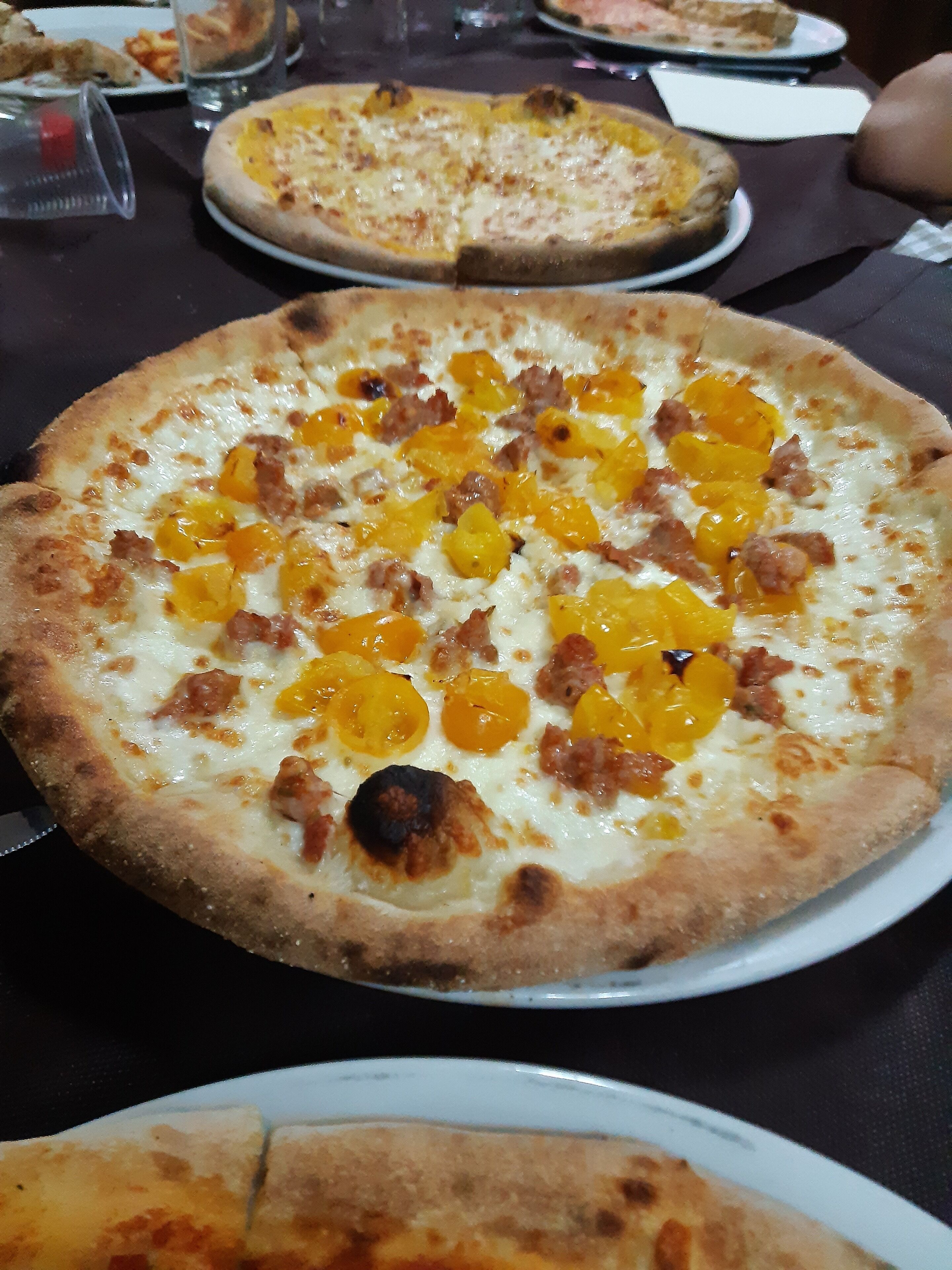 A pizza with yellow bell peppers and ham on a white plate.