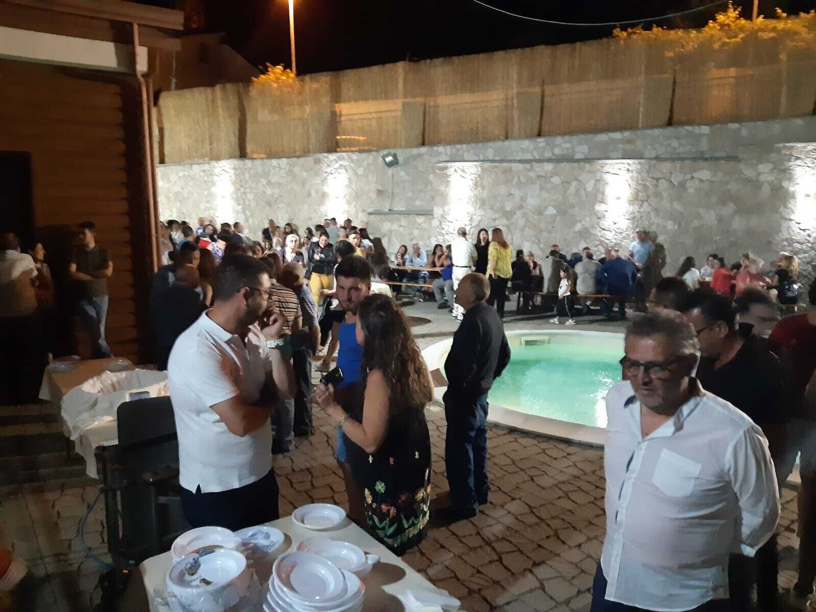 A crowded outdoor area with a pool, stone walls, and tables with dishes.