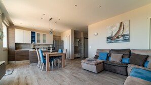 En moderne stue med en hjørnesofa, et spiseområde med et træbord og stole, samt et køkken i baggrunden.
