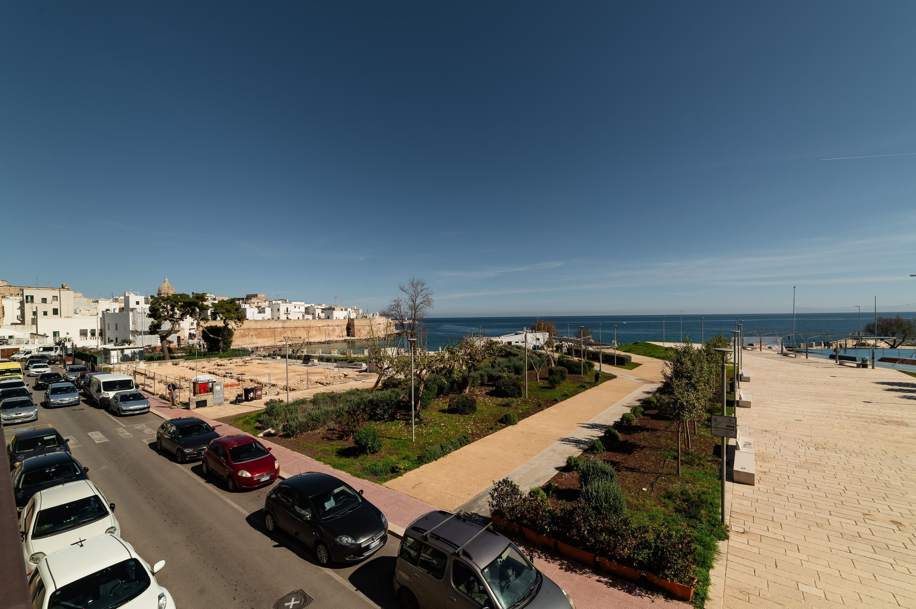 Eine Küstenstraße mit parkenden Autos, einem Bürgersteig und Blick auf das Meer.
