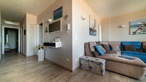 En moderne stue med en hjørnesofa, et lille bord og et vægmonteret tv. Der er en gang, der fører til et andet værelse.