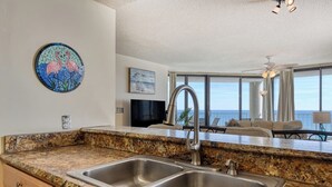 A kitchen with granite countertops, stainless steel sinks, and a dining area with a view of the ocean. - One Ocean Place 1105- Three Bedroom, Three Bath Oceanfront Condo (Garden City Beach)