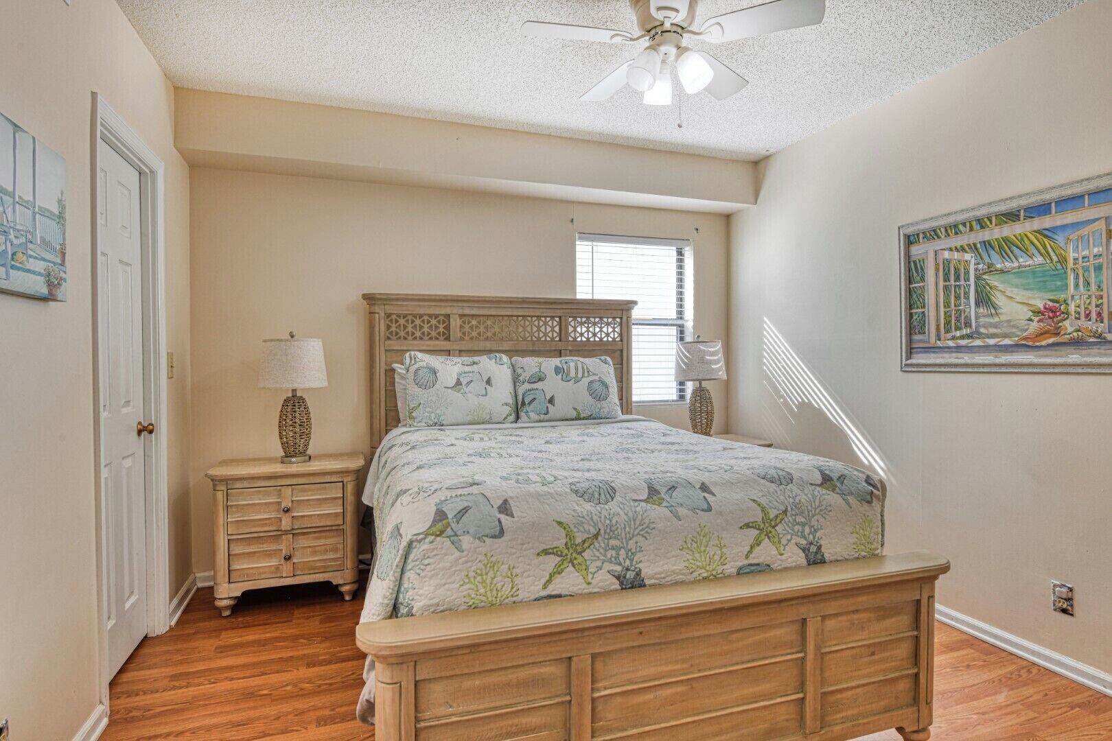 A bedroom with a wooden bed, a nightstand, a lamp, a window with blinds, and a painting on the wall.