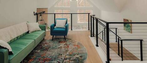 A spacious loft with a green sofa, a blue armchair, and a patterned rug.