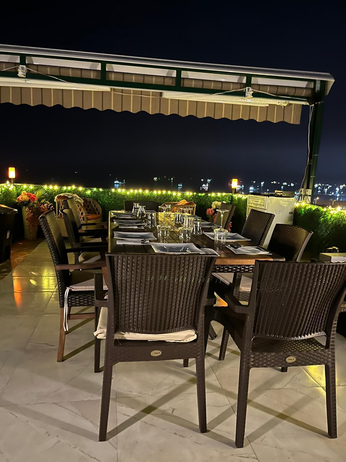 An outdoor dining area with a covered patio, tables set with chairs, and a city view in the background.