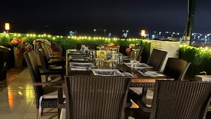 An outdoor dining area with a covered patio, tables set with chairs, and a city view in the background. - The Mua Luxury Homes (Istanbul)