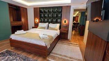 A modern bedroom with a large bed, wooden headboard, bedside tables with lamps, and a view into the dining area.