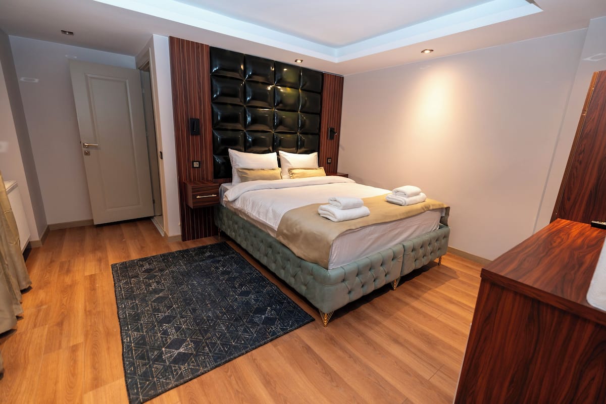 A modern bedroom with a tufted headboard, a large bed with a beige bedspread, and a dark patterned rug.