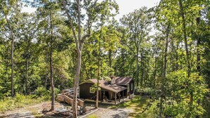 Un chalet rustique doté d’une véranda et d’une petite terrasse, entouré d’une forêt dense.